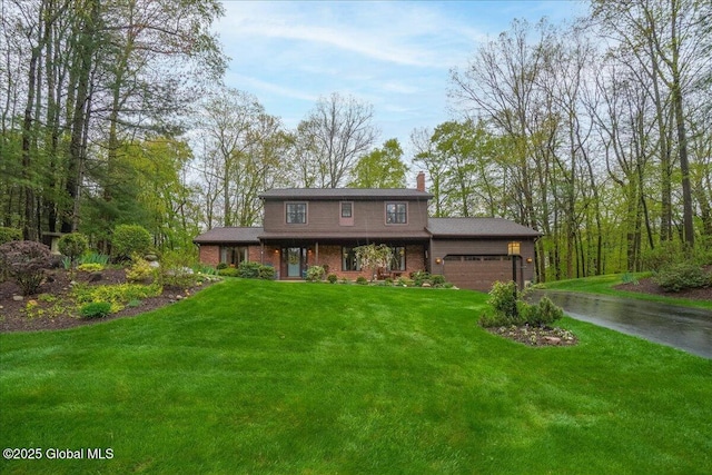 view of front of home featuring an attached garage, brick siding, driveway, a front yard, and a chimney