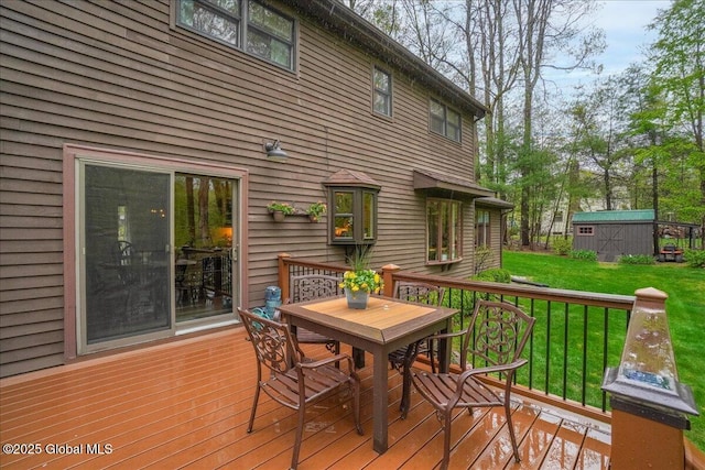 wooden deck featuring an outdoor structure, outdoor dining space, a shed, and a lawn
