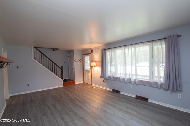 unfurnished living room featuring wood finished floors, stairway, and baseboards