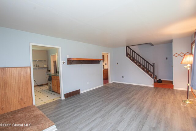 unfurnished living room with stairway, wood finished floors, and baseboards