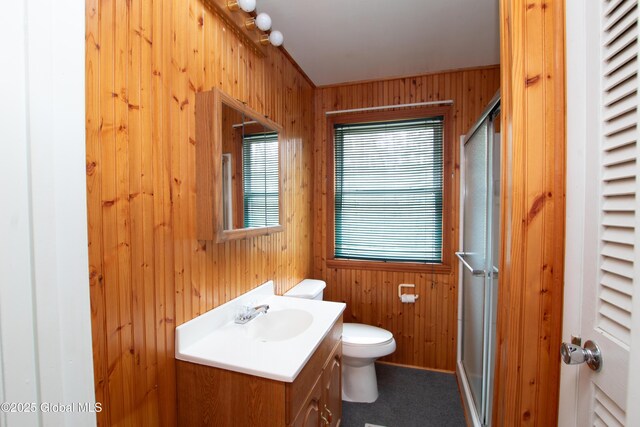 full bathroom featuring wooden walls, vanity, a stall shower, toilet, and baseboards