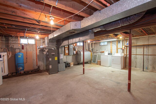 basement featuring heating fuel, a water pressure tank, washer and clothes dryer, heating unit, and water heater