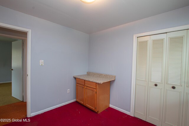 unfurnished bedroom featuring dark colored carpet, baseboards, and a closet