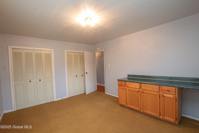 unfurnished bedroom featuring light carpet, multiple closets, and baseboards