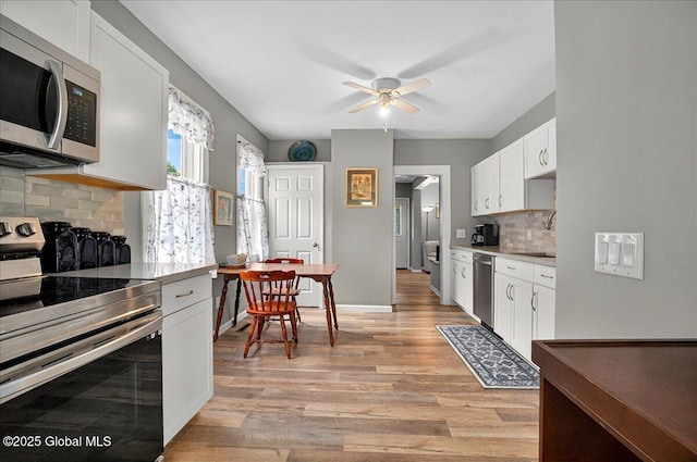 kitchen with appliances with stainless steel finishes, a ceiling fan, backsplash, light wood-type flooring, and white cabinetry