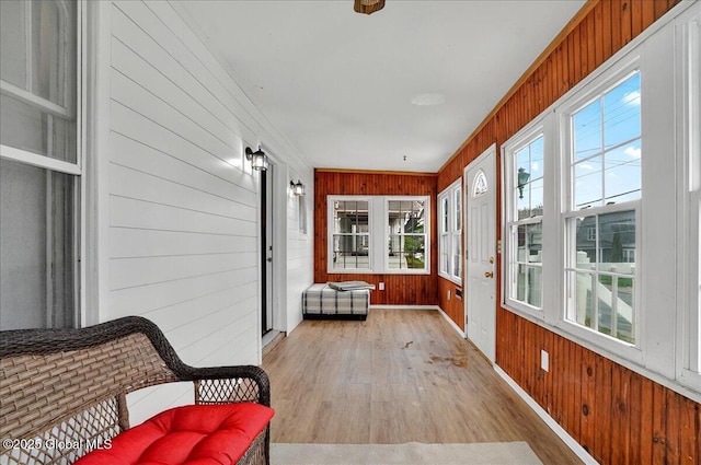 sunroom featuring wood finished floors, wooden walls, and baseboards