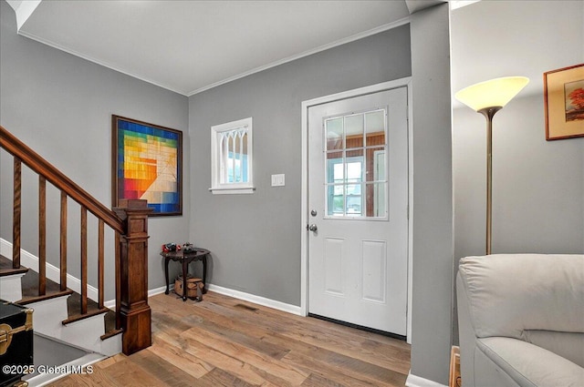 foyer entrance featuring crown molding, wood finished floors, stairway, and baseboards