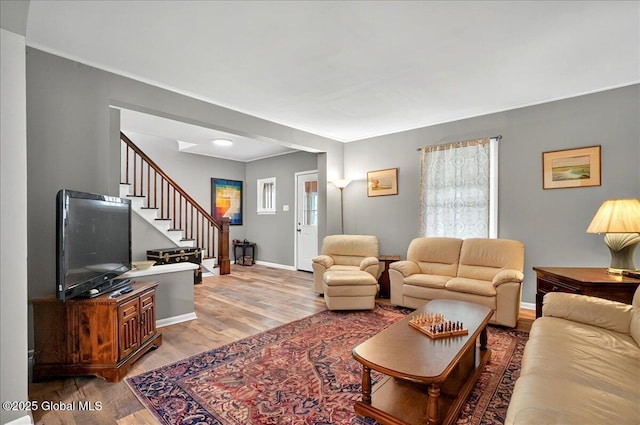 living room with stairs, ornamental molding, light wood-type flooring, and baseboards
