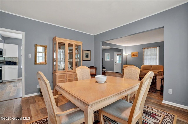 dining area with light wood-style floors, baseboards, and crown molding