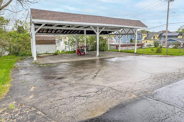 view of parking with a carport, driveway, and fence