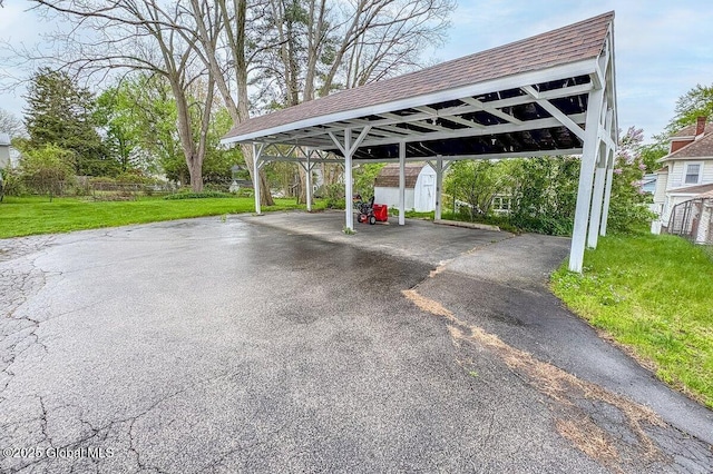 view of parking featuring a detached carport, asphalt driveway, and a storage shed