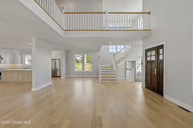 foyer featuring a high ceiling, light wood-style flooring, stairway, and plenty of natural light