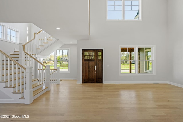 entrance foyer featuring light wood finished floors, baseboards, stairs, recessed lighting, and a towering ceiling