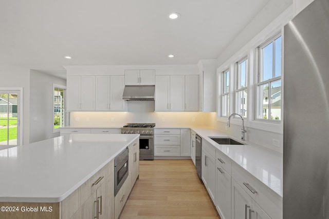 kitchen featuring stainless steel appliances, a sink, a kitchen island, light countertops, and recessed lighting