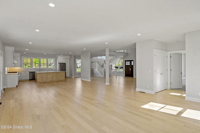unfurnished living room with recessed lighting, baseboards, light wood-style flooring, stairway, and a sink