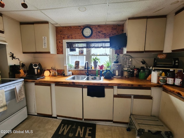 kitchen with butcher block counters, a sink, white range with electric cooktop, a paneled ceiling, and cream cabinets