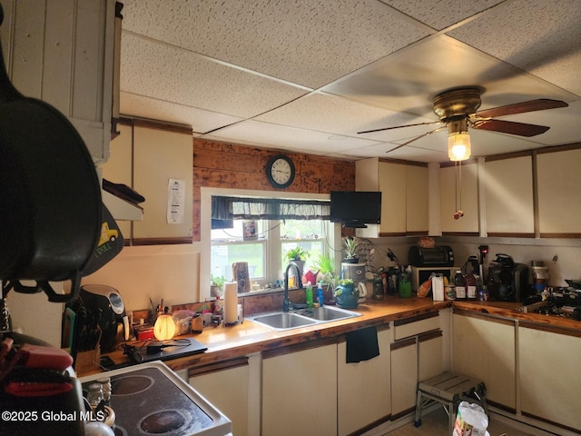 kitchen with a drop ceiling, wooden counters, ceiling fan, a sink, and range with electric stovetop