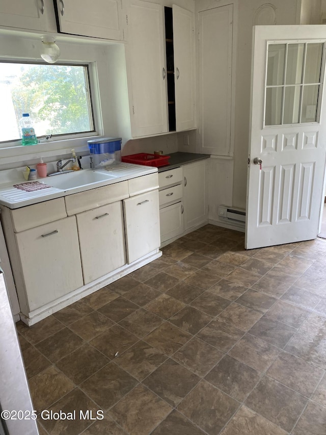 kitchen featuring white cabinetry, stone finish floor, a baseboard radiator, and a sink
