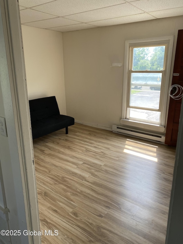 unfurnished room with light wood-style flooring, baseboard heating, and a paneled ceiling