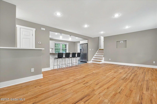 unfurnished living room featuring baseboards, stairs, and light wood-style floors
