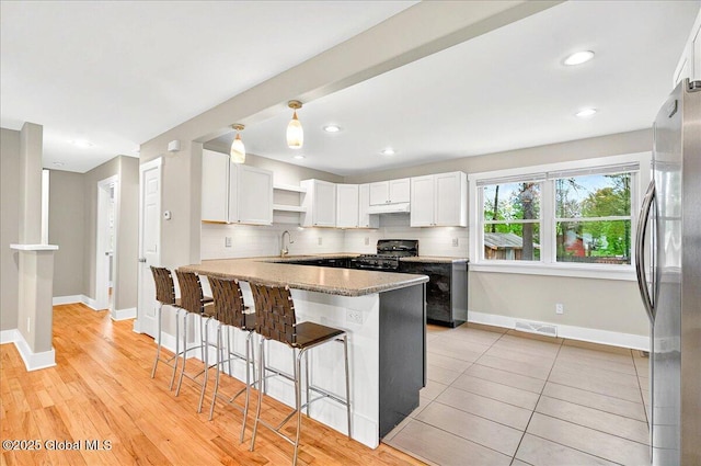 kitchen with a peninsula, white cabinetry, visible vents, baseboards, and black gas stove