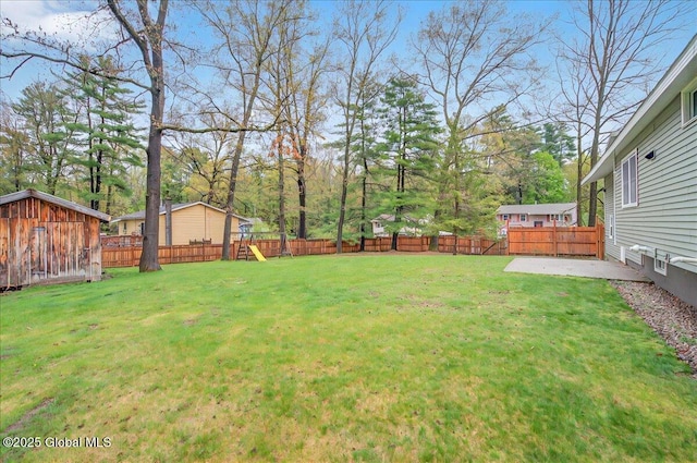 view of yard with a patio area, a shed, an outbuilding, a fenced backyard, and a playground