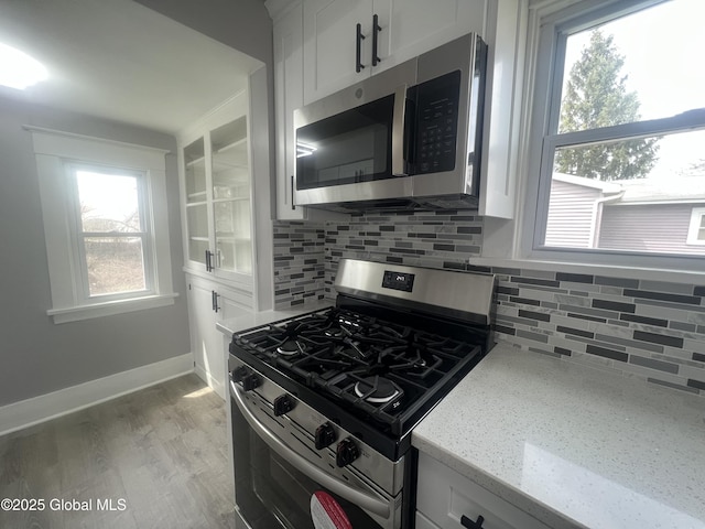 kitchen with appliances with stainless steel finishes, tasteful backsplash, white cabinets, light stone counters, and light wood finished floors