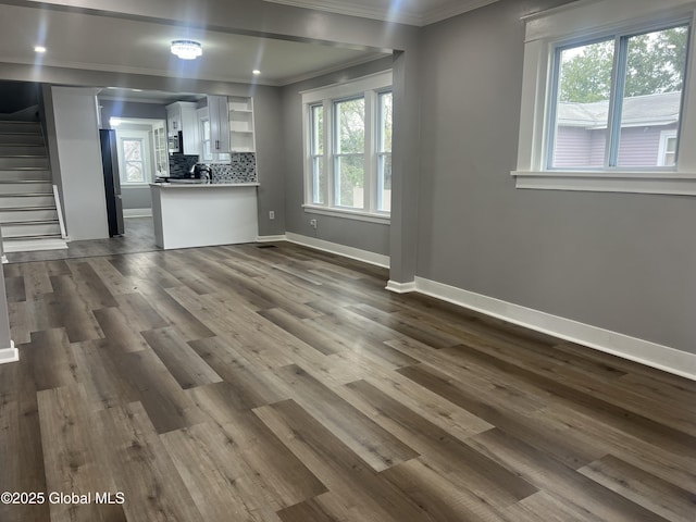 unfurnished living room with stairs, ornamental molding, baseboards, and dark wood-style flooring