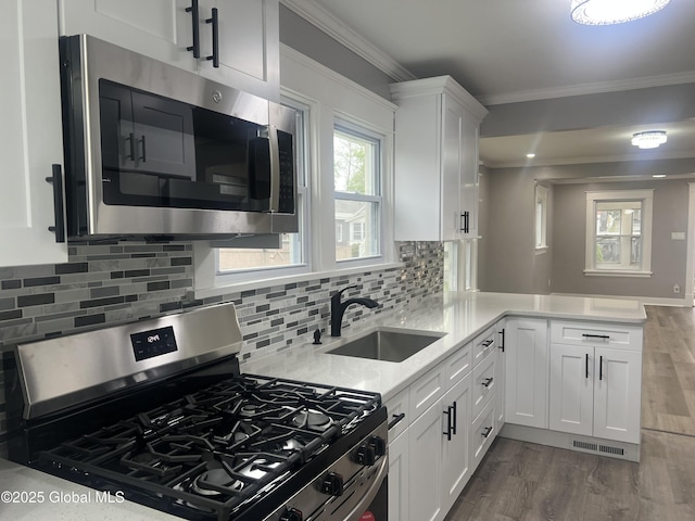 kitchen featuring stainless steel appliances, a sink, crown molding, white cabinetry, and a peninsula