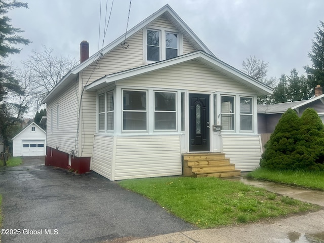bungalow-style house with entry steps, driveway, a detached garage, a chimney, and an outdoor structure
