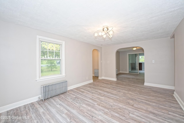 unfurnished room featuring radiator, arched walkways, light wood-type flooring, and a chandelier