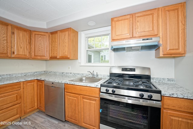 kitchen featuring under cabinet range hood, stainless steel appliances, a sink, light wood-style flooring, and light stone countertops