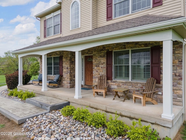 property entrance featuring covered porch, stone siding, and roof with shingles