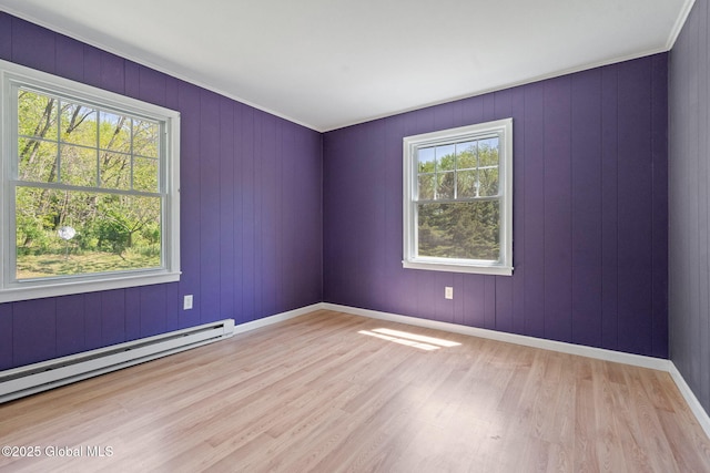 unfurnished room featuring a baseboard heating unit, plenty of natural light, wood finished floors, and baseboards