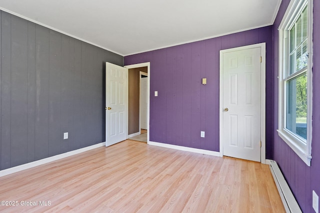 unfurnished bedroom featuring baseboard heating, light wood finished floors, crown molding, baseboards, and wood walls