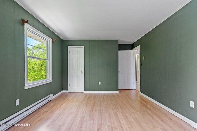 unfurnished room with a baseboard heating unit, light wood finished floors, baseboards, and crown molding