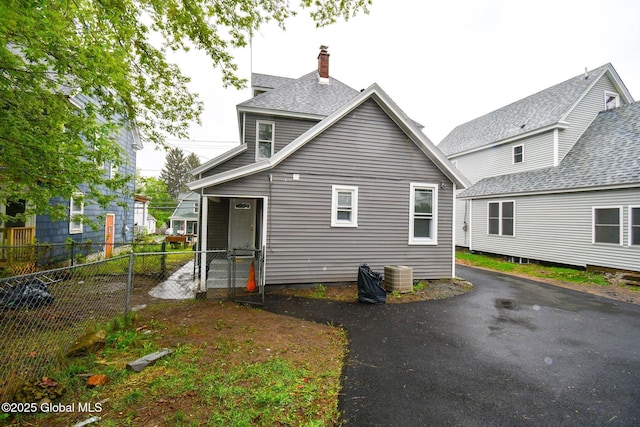 back of property with central AC unit, fence, and a chimney