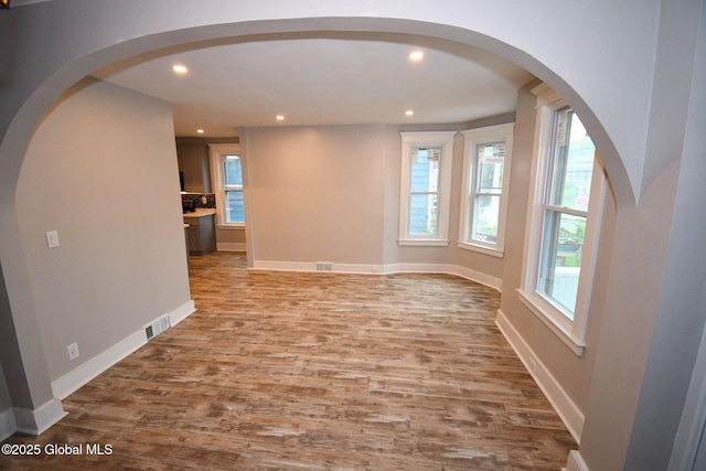 unfurnished room featuring wood finished floors, visible vents, recessed lighting, arched walkways, and baseboards