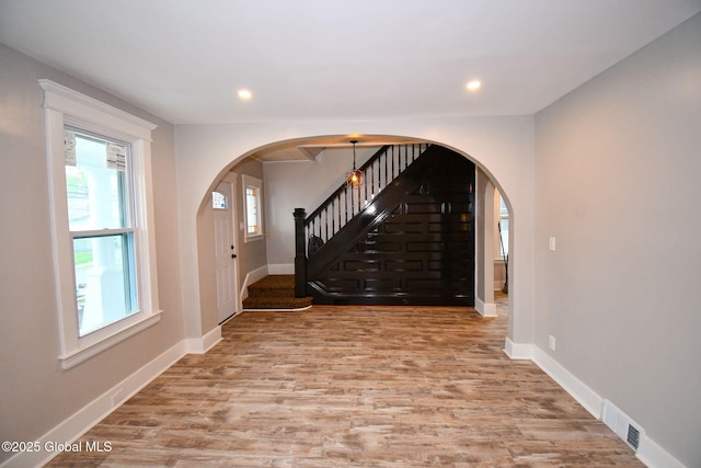 foyer entrance with arched walkways, stairway, visible vents, and wood finished floors