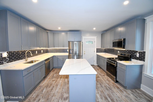 kitchen with decorative backsplash, a sink, gray cabinets, appliances with stainless steel finishes, and a kitchen island