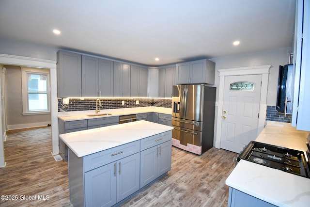 kitchen featuring a sink, stainless steel appliances, tasteful backsplash, gray cabinets, and wood finished floors