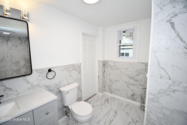 bathroom with toilet, marble finish floor, tile walls, and vanity