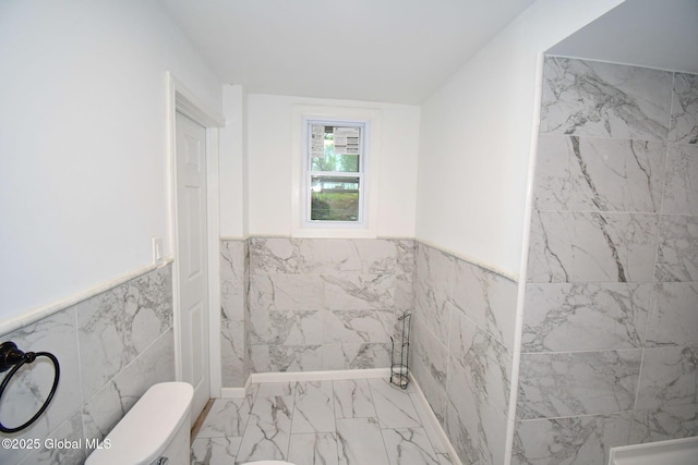 bathroom with wainscoting, toilet, tile walls, and marble finish floor