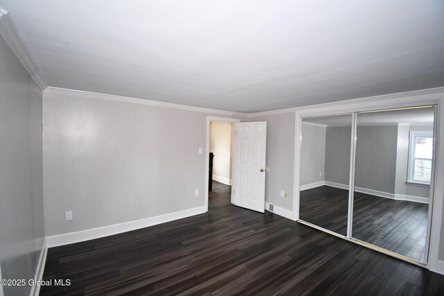unfurnished bedroom with a closet, dark wood finished floors, baseboards, and ornamental molding
