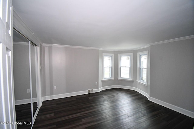 spare room featuring baseboards, dark wood-style flooring, crown molding, and visible vents