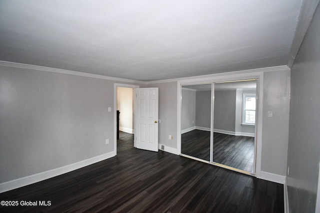 unfurnished bedroom featuring ornamental molding, baseboards, dark wood-type flooring, and a closet
