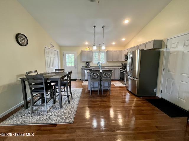 kitchen featuring stainless steel appliances, vaulted ceiling, dark wood-style flooring, a kitchen island, and a breakfast bar area