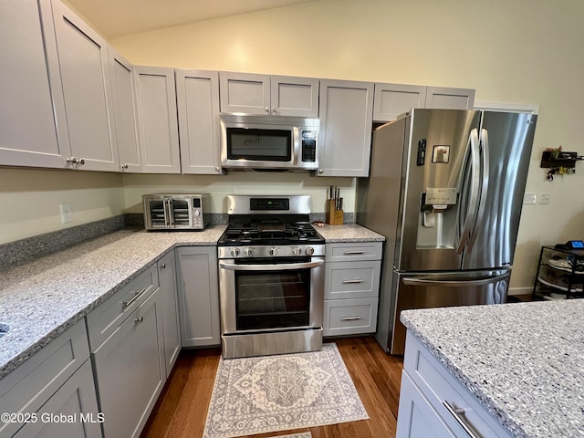 kitchen featuring stainless steel appliances, gray cabinets, lofted ceiling, dark wood-type flooring, and light stone countertops