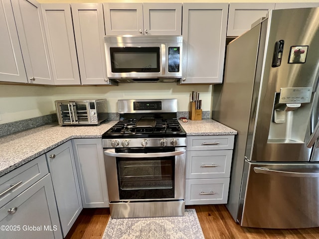 kitchen featuring stainless steel appliances, dark wood finished floors, gray cabinetry, and light stone counters