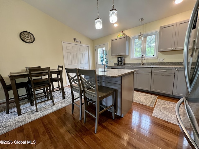 kitchen featuring gray cabinetry, a sink, freestanding refrigerator, a breakfast bar, and lofted ceiling
